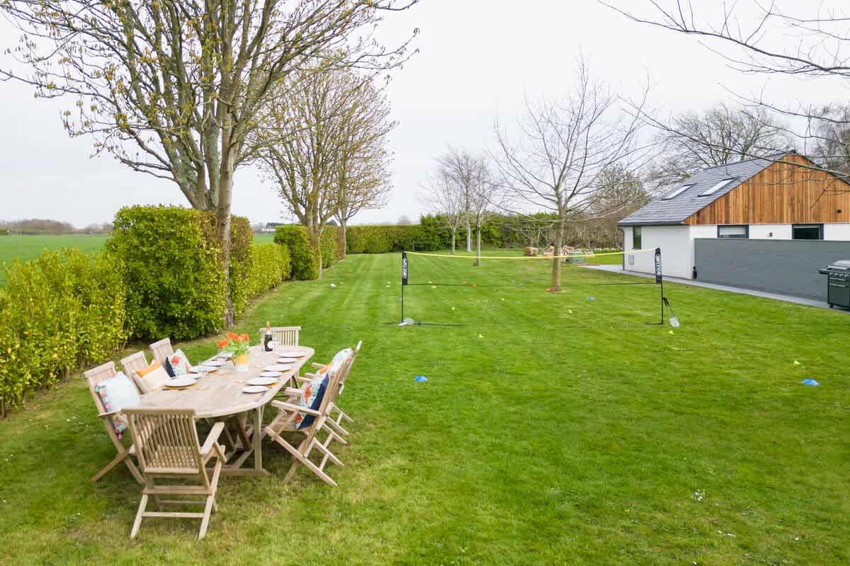 Expansive outdoor space with a dining area under the trees, perfect for al fresco meals. The large lawn includes recreational setups for activities and games, offering relaxation and fun in a serene countryside setting. Ideal for families or groups