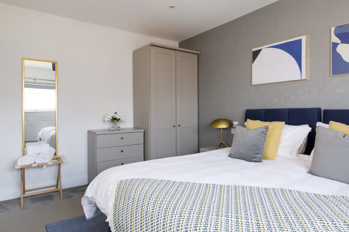 Bedroom 3 - Cedar House: Elegant bedroom with a king-size bed, sleek wardrobe, and contemporary decor. Features a full-length mirror, soft lighting, and vibrant accents, offering a stylish and comfortable space for relaxation.