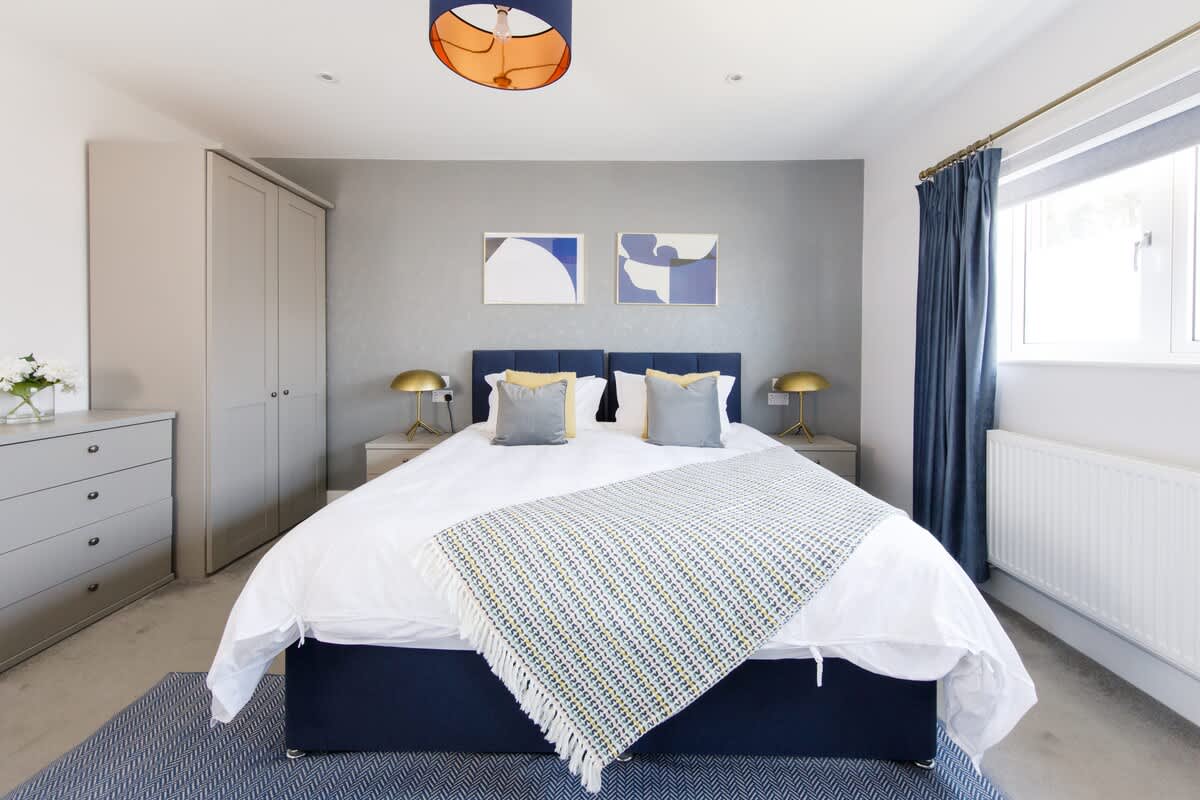 Bedroom 3 - Cedar House: Spacious bedroom with a luxurious king-size bed, stylish decor, and calming blue accents. Features soft linens, modern artwork, ample storage, and natural light, creating a serene and comfortable retreat.