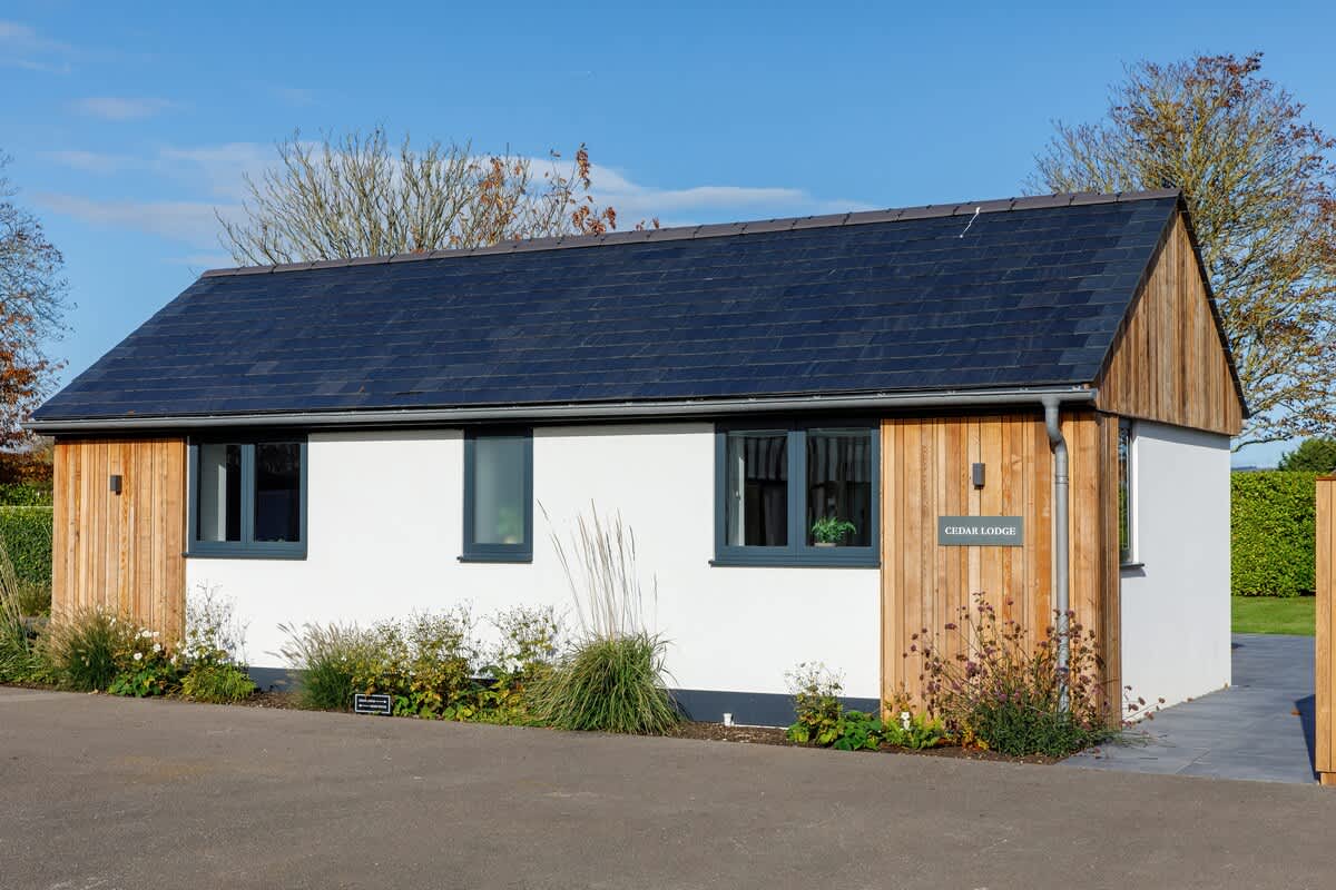Cedar Lodge: A charming, modern retreat with a sleek design, solar-paneled roof, and surrounded by lush greenery. This cozy space offers the perfect blend of comfort and sustainability for a relaxing countryside escape.