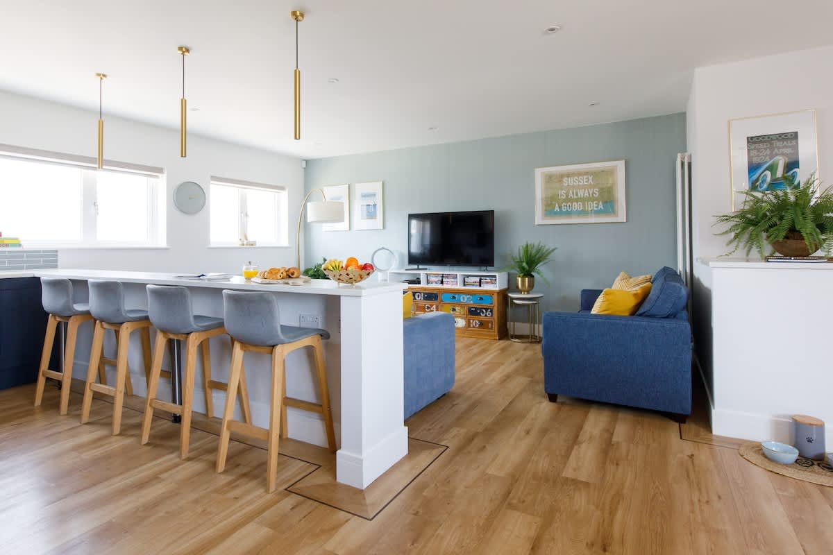 Cedar House: Spacious open-plan kitchen & living area with a breakfast bar, stylish seating, & cozy lounge. Features modern decor, a flat-screen TV, & natural light streaming through large windows, creating a perfect space for relaxing & entertaining