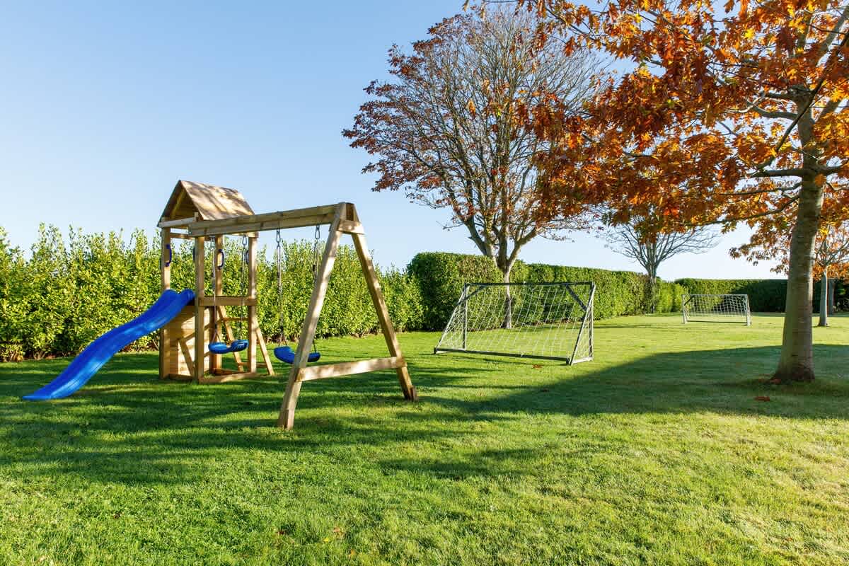 Enjoy outdoor fun at Cedar House with a play area featuring a wooden climbing frame, swings, and slide. Perfectly complemented by lush green lawns and soccer goals, it's an ideal space for children and family activities in a serene setting.