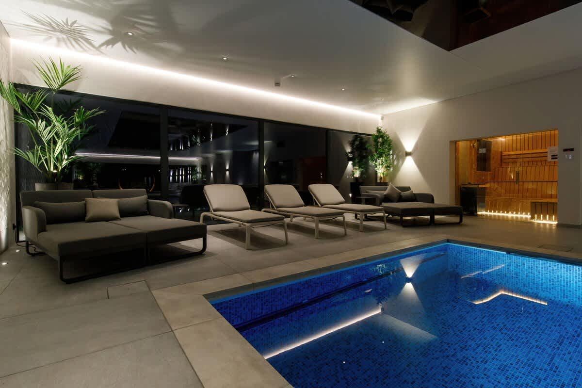 Luxurious indoor pool with loungers, ambient lighting, and lush greenery. Includes a sauna for ultimate relaxation. Perfect for unwinding and enjoying a tranquil, spa-like experience during your stay (extra charges apply)