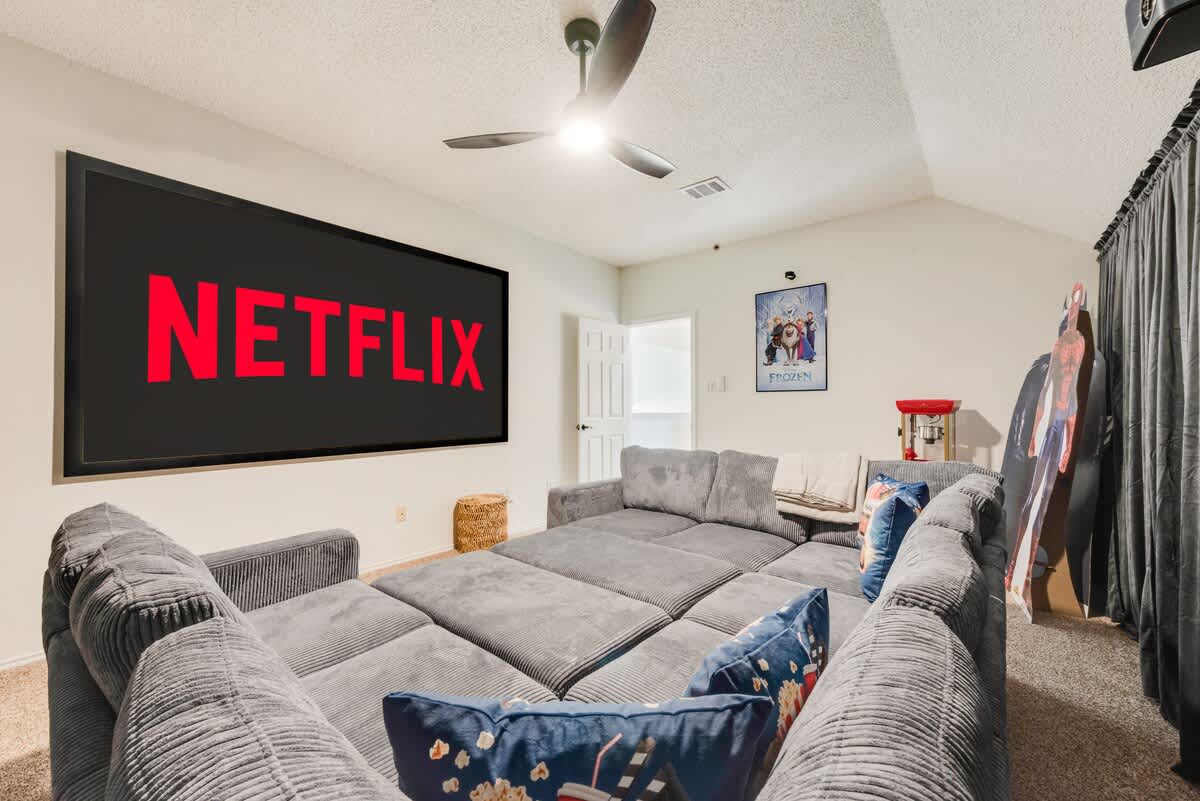 This cinema room doubles as Bedroom 5, featuring a large sectional sofa/bed and a big screen for streaming. Fun decor includes movie posters and a popcorn machine (decor only), creating a cozy space to relax.