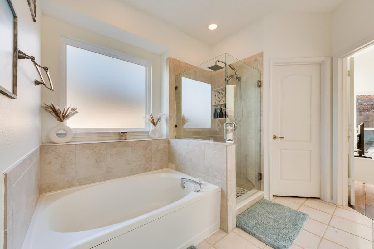 This modern bathroom features a bathtub and shower with a rainfall showerhead and glass enclosure. 