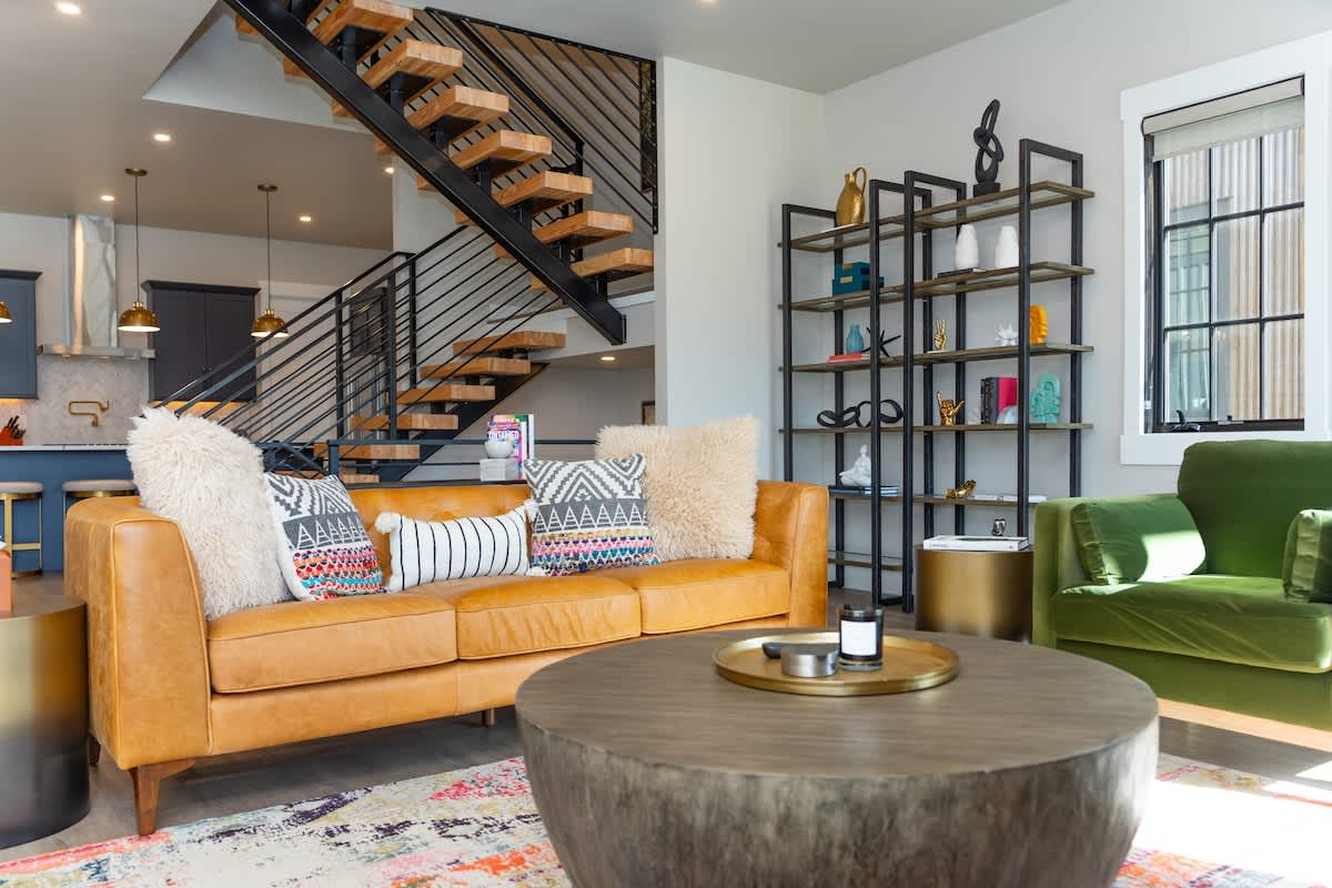 - Stylish living room with leather sofa colorful pillows & modern staircase backdrop
- Open shelving adds decorative storage while large windows fill the space with light
- Perfect for relaxing or socializing in a bright contemporary mountain retreat