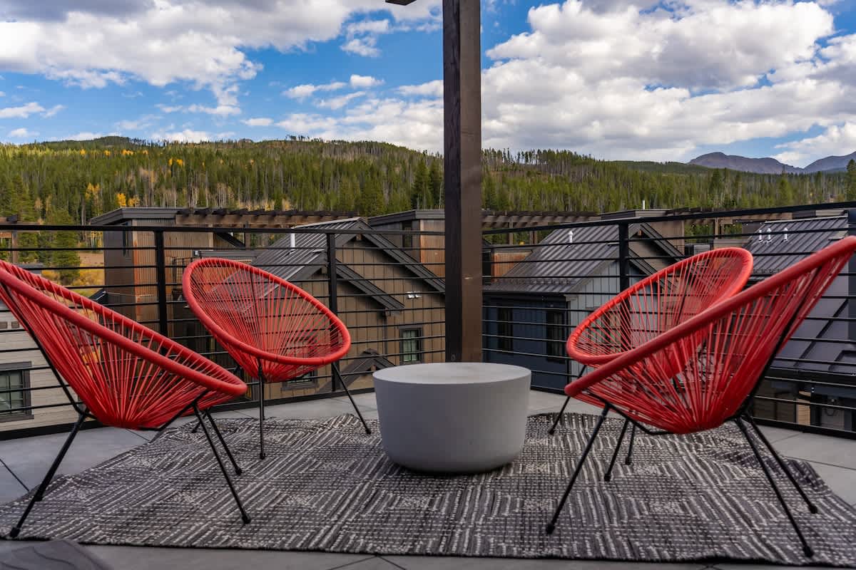 - Stunning rooftop seating area with panoramic views of the mountains
- Three modern red chairs surround a sleek round table on an outdoor rug
- Ideal place to unwind while enjoying the crisp mountain air