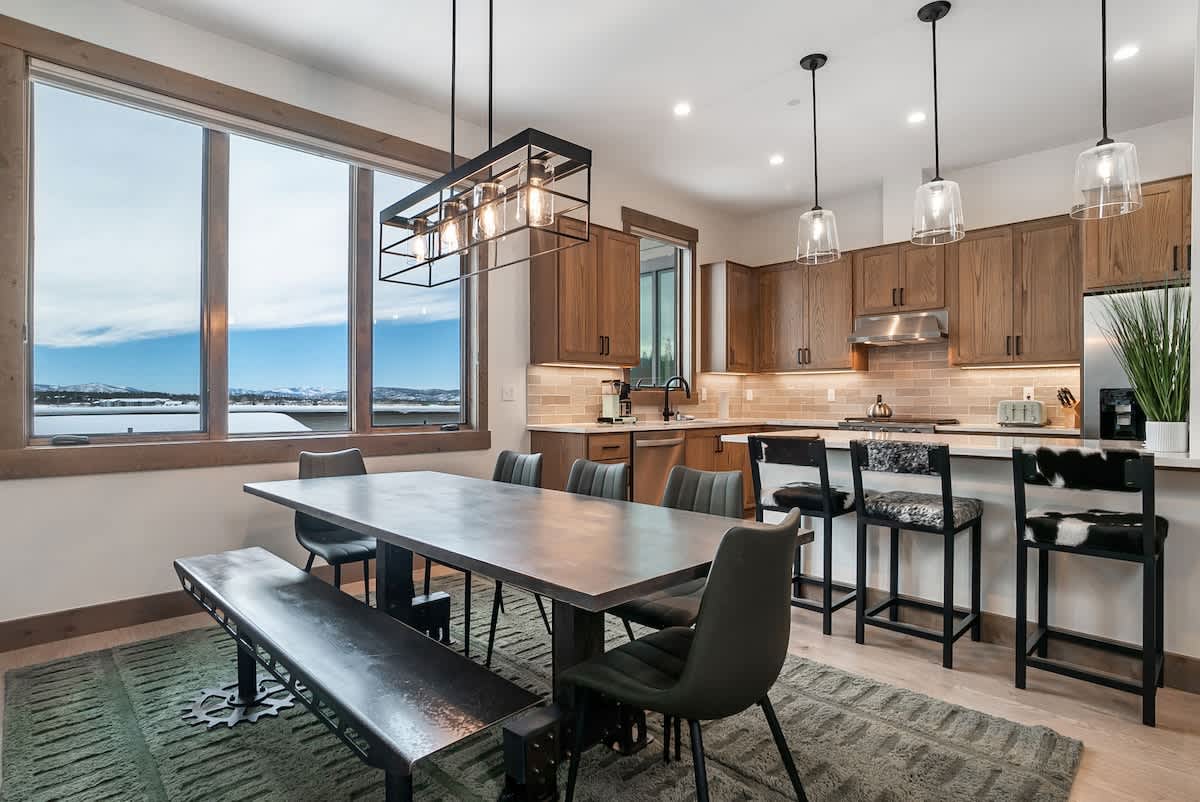 - Dining space with a mix of chairs and bench seating beside a bright kitchen
- Large windows showcase the beauty of the surrounding landscape
- Pendant lights over the island add style and warmth to the open space