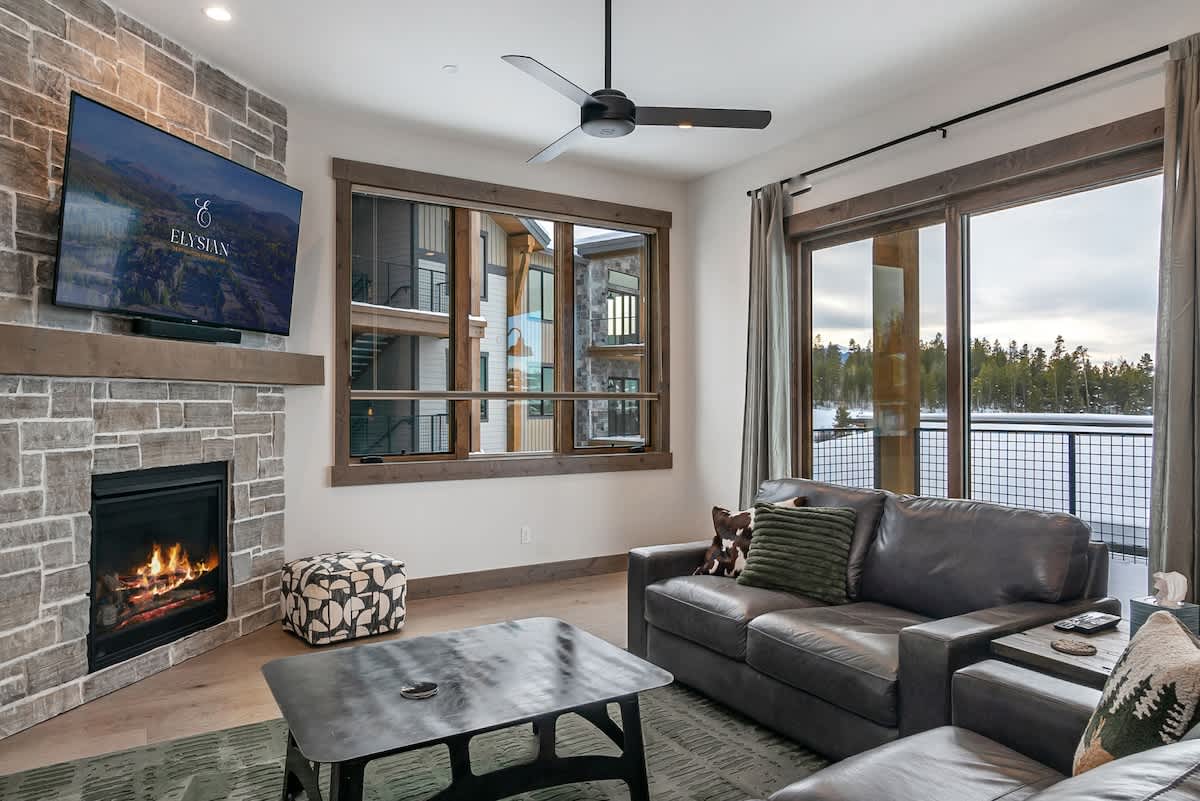 - Cozy living area with stone fireplace and wall mounted TV for relaxing nights
- Large windows and sliding doors open to a balcony with scenic mountain views
- Comfortable leather seating offers a perfect spot to unwind after adventures