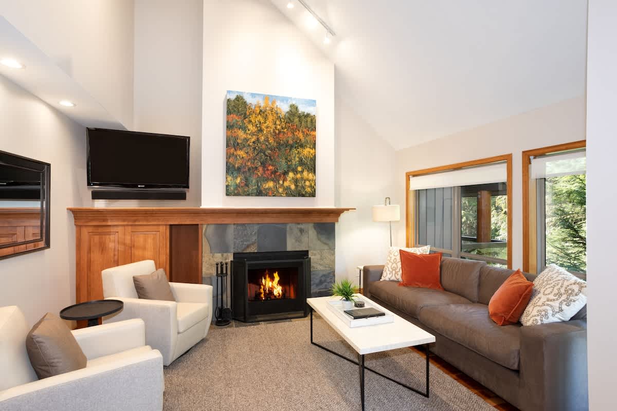 - Warm up by the glowing fireplace in this inviting modern mountain retreat 
- Spacious living room with soft seating, large windows, and forest scenery 
- Perfect for relaxing evenings after skiing or exploring the mountain trails 