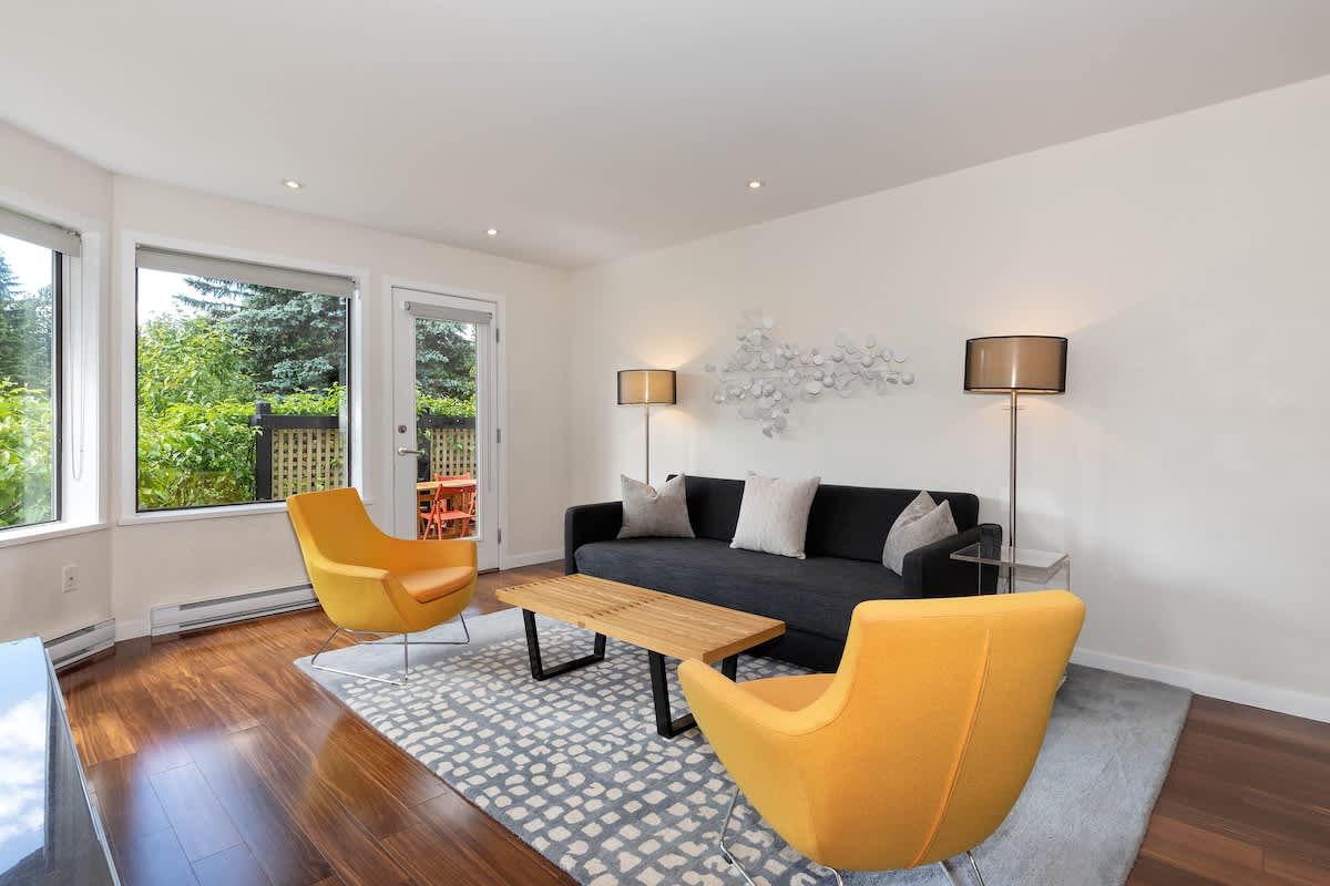 Bright living area w/ large windows, warm wood floors, and inviting seating perfect for relaxing together.