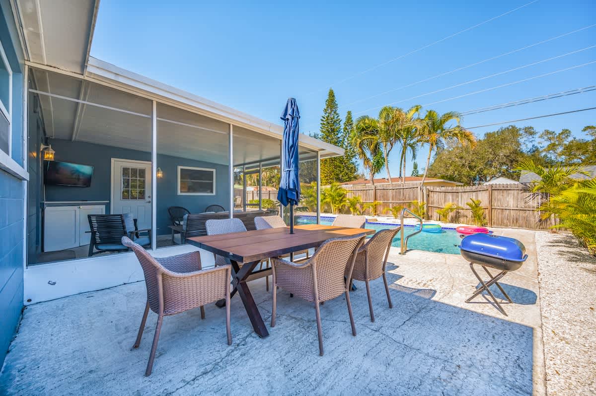 The outdoor dining table accommodates six people comfortably, with an umbrella providing shade, and a charcoal grill with charcoal nearby.