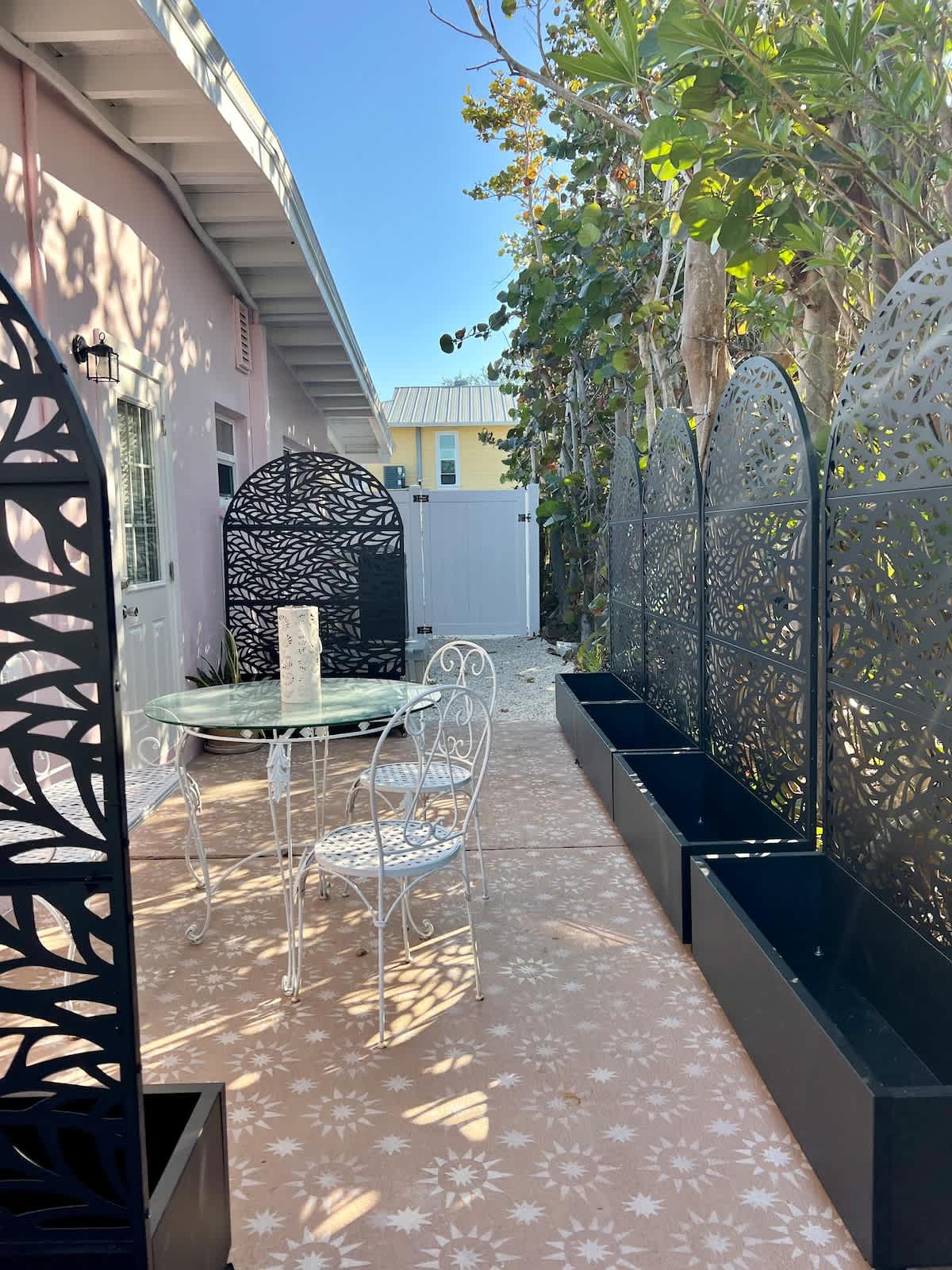 OUR LITTLE SECRET GARDEN. UPDATED SIDE PATIO.  PLANTS COMING SOON. THERE ARE SOLAR POWERED STRING LIGHTS (not pictured) WE ADDED FOR EXTRA AMBIENCE! SMALL BISTRO TABLE TO ENJOY A CUP OF COFFEE OR GLASS OF WINE UNDER THE STRING LIGHTS.