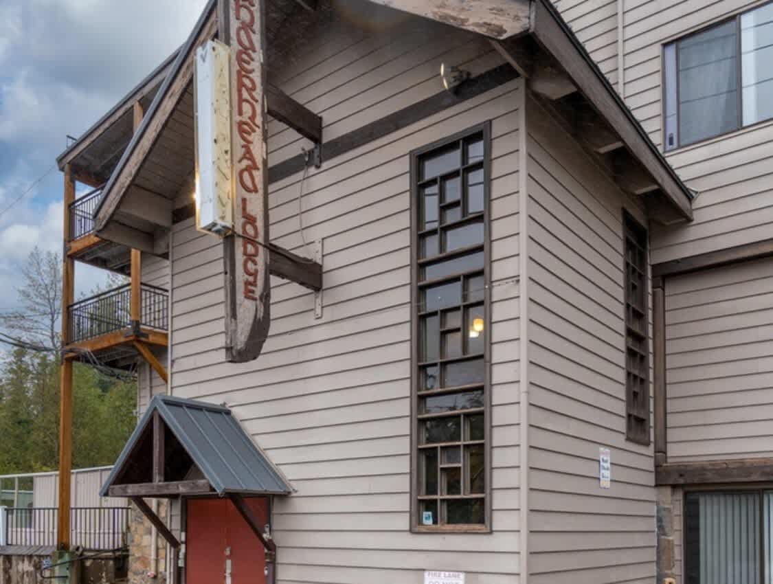 A close-up exterior view of the lodge, highlighting light brown siding, a small covered entrance with a red door, tall multi-pane windows, and a vintage "Thunderhead Lodge" sign hanging from the building, reflecting its rustic charm.
