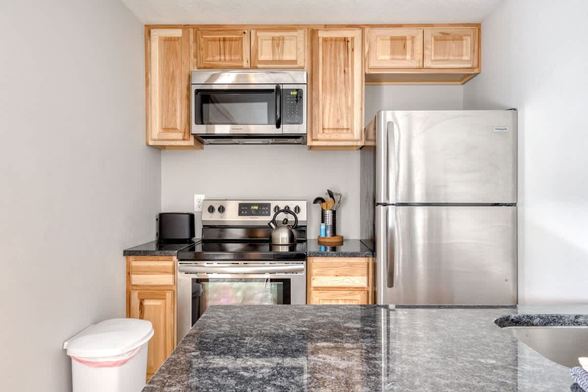 Detailed view of the kitchen showcasing stainless steel appliances like the microwave, stove, and refrigerator, complemented by light wood upper and lower cabinets and dark countertops.