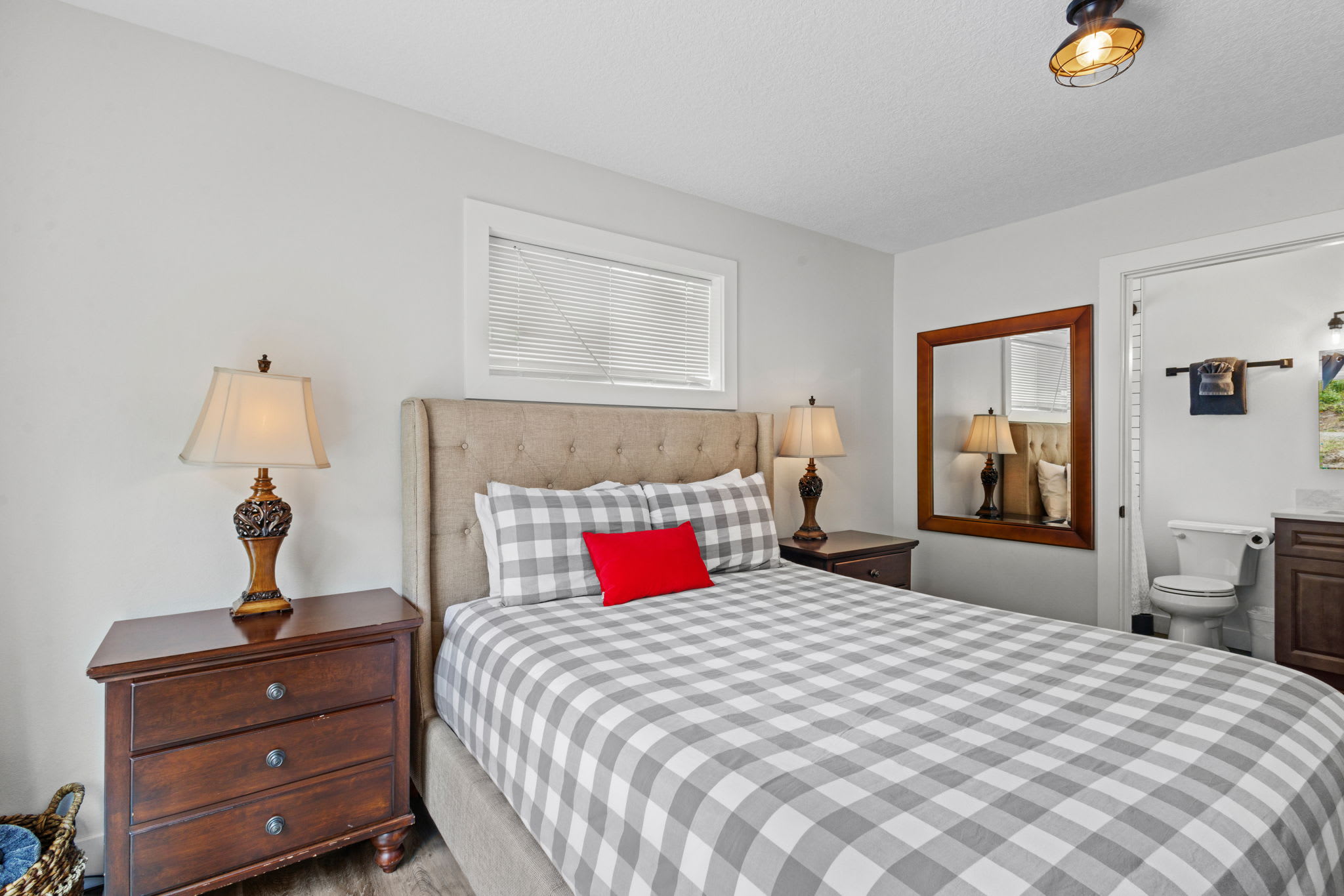 Bedroom featuring a queen-sized bed with a tufted headboard and a grey and white checkered duvet, flanked by dark wood nightstands with lamps, and a window with blinds.