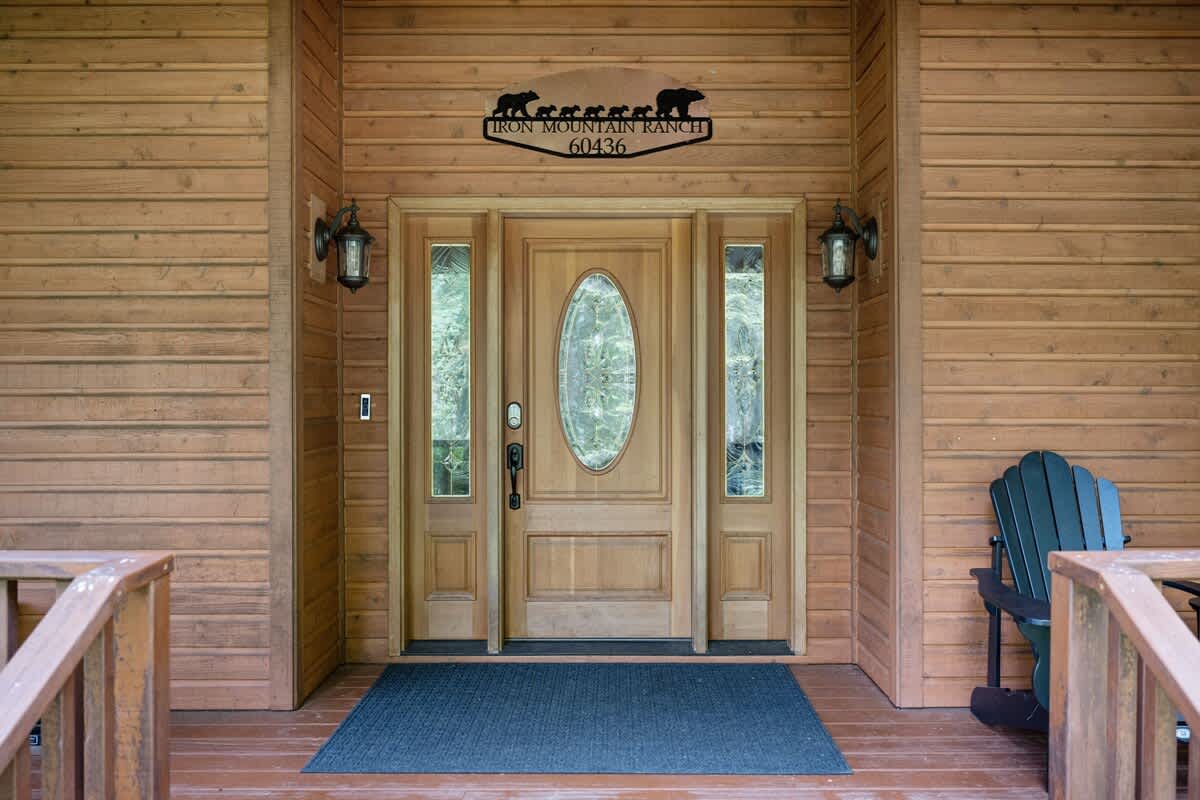 The main entrance features a light wood double door with an oval glass insert, flanked by two sidelights and outdoor sconces, beneath a metal sign reading "IRON MOUNTAIN RANCH".