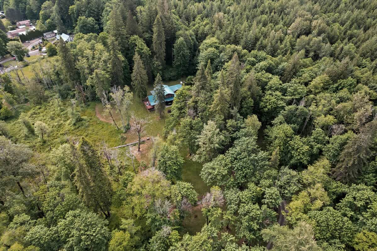 Broad aerial perspective showcasing the lodge nestled deep within a vast expanse of verdant forest, highlighting the property's secluded natural setting and proximity to other homes.