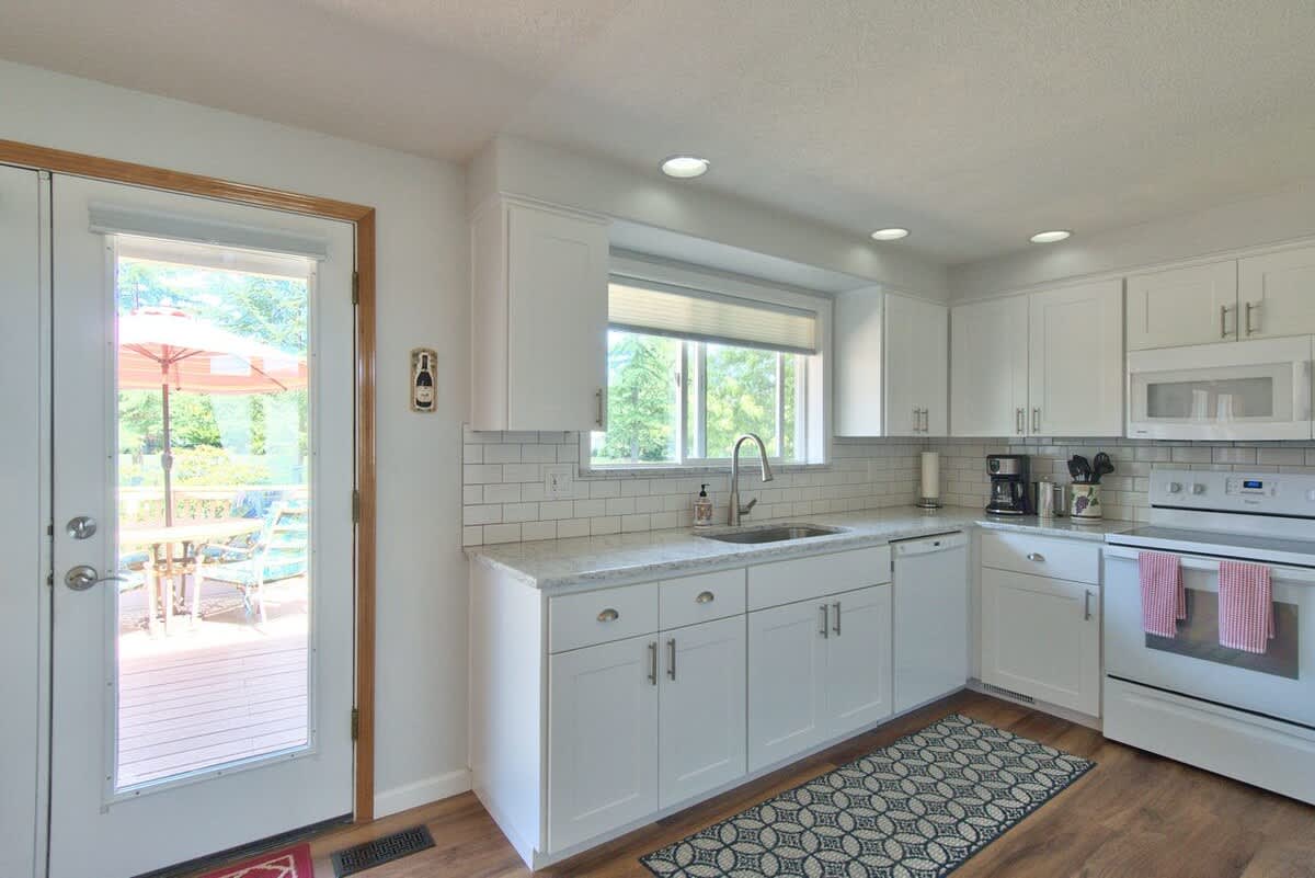 Bright kitchen featuring white cabinets, light countertops, and a white subway tile backsplash, with a white range and microwave, and a glass-paned door opening to an outdoor deck.