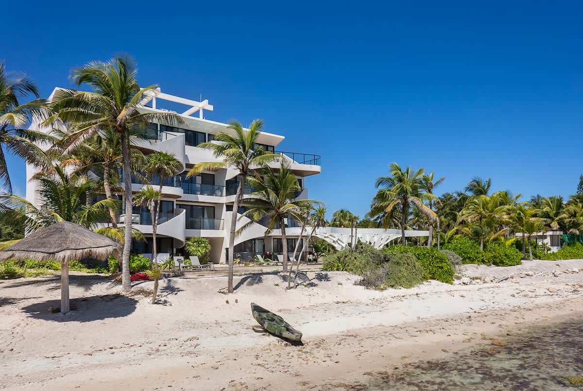 A view of the complex adorned with palm trees, lush vegetation, and soft sand, creating a picturesque and tropical atmosphere.
