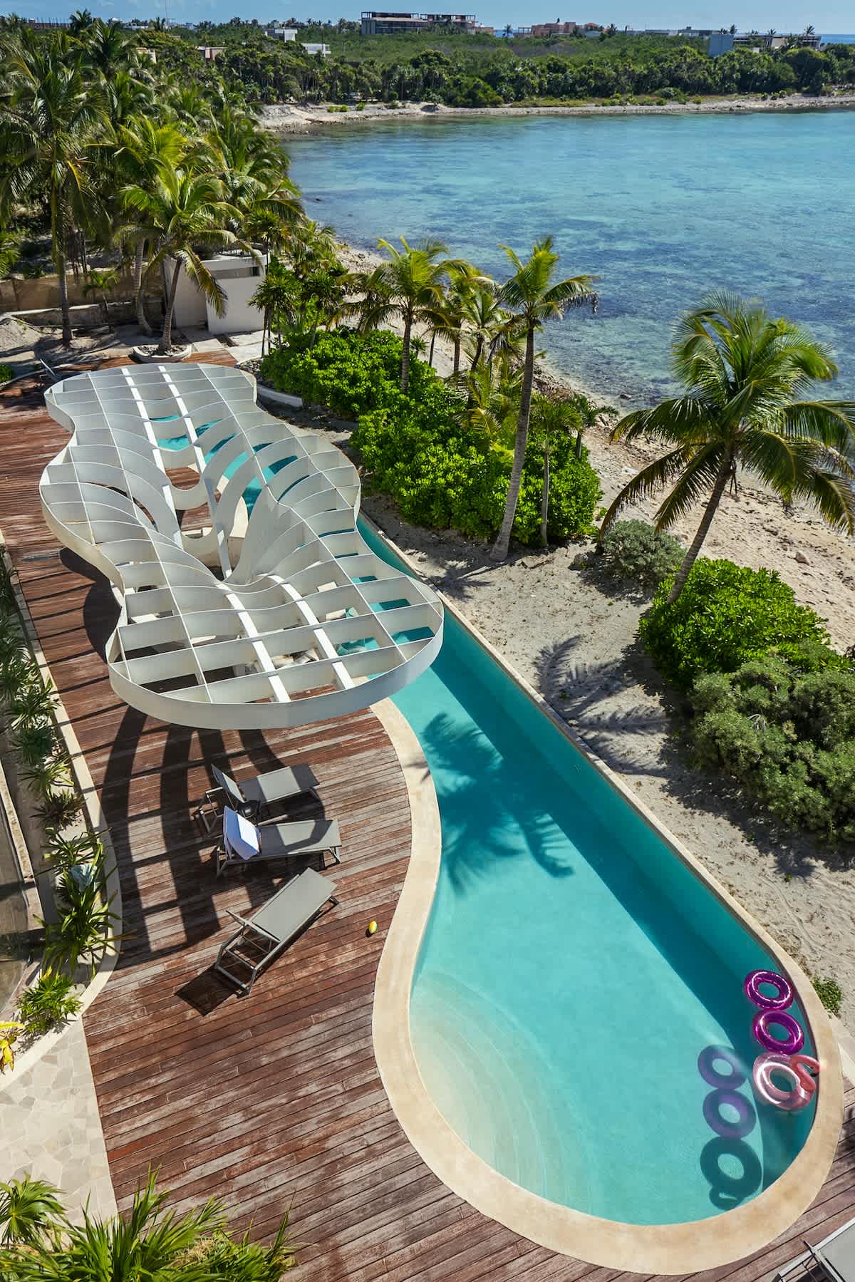 An aerial view of the pool, beautifully framed by the sea, sand, and lush vegetation, creating a stunning and serene landscape.