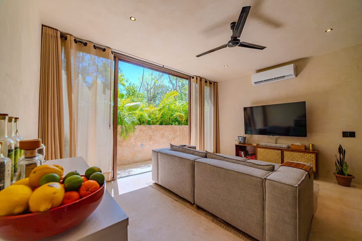 Spacious and bright living room with Smart TV, comfortable seating, and large windows overlooking the lush Tulum jungle.