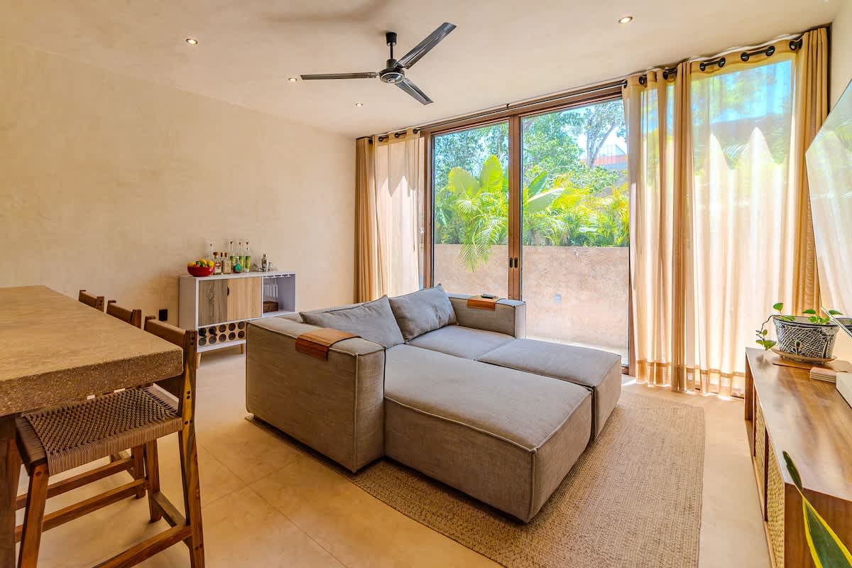 Spacious and bright living room with Smart TV, comfortable seating, and large windows overlooking the lush Tulum jungle.