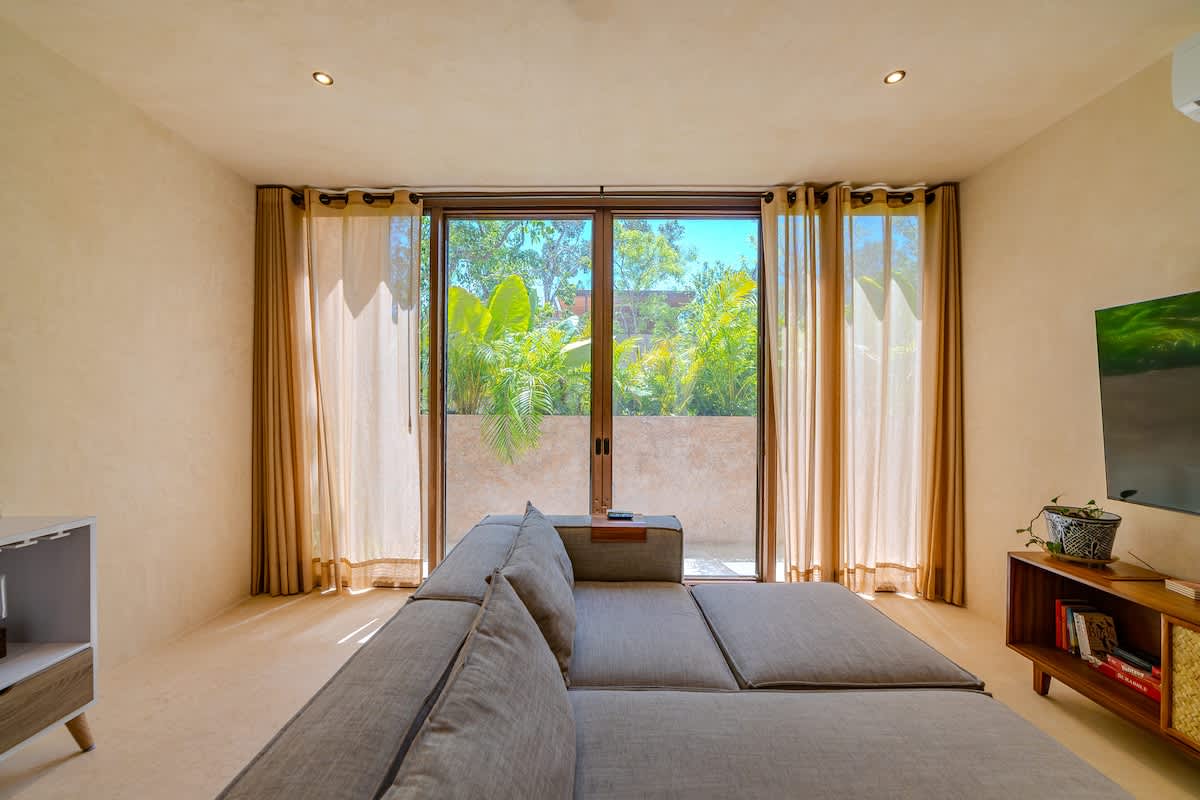 Spacious and bright living room with Smart TV, comfortable seating, and large windows overlooking the lush Tulum jungle.