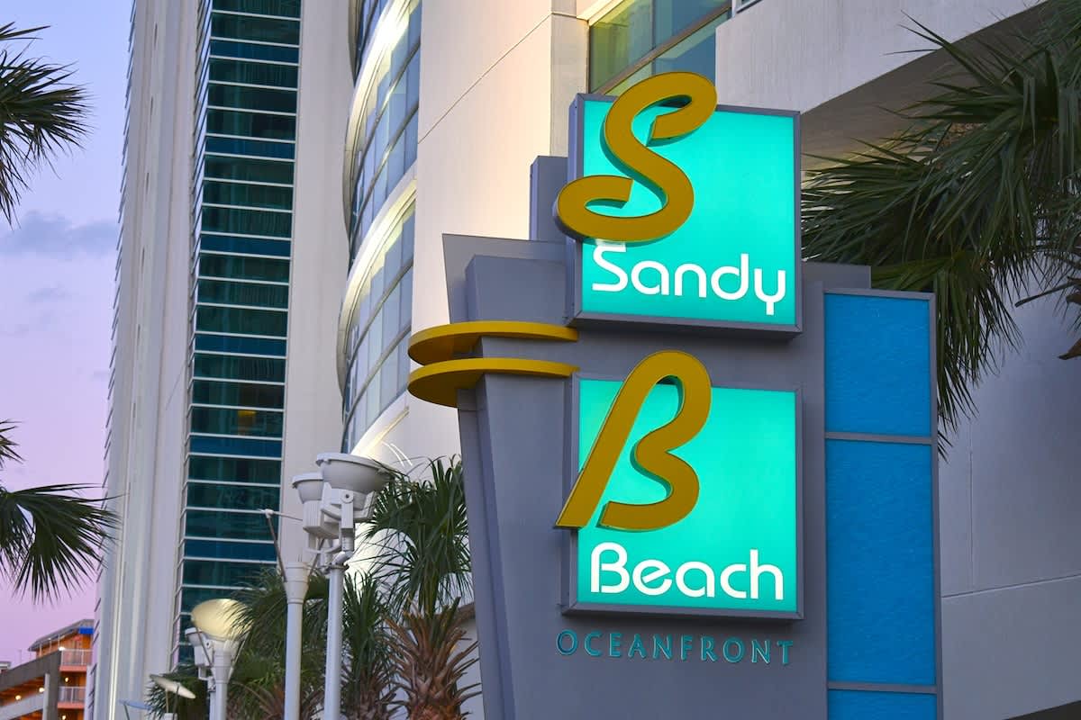 - Bright Sandy Beach resort sign welcomes guests to oceanfront condos   - Prime Myrtle Beach location with easy access to beach attractions   - Iconic sign marks entry to a memorable coastal vacation experience