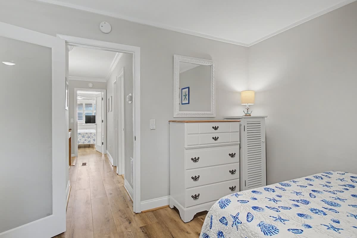 Your serene bedroom features elegant coastal-themed linens and a charming white dresser for storing your belongings.