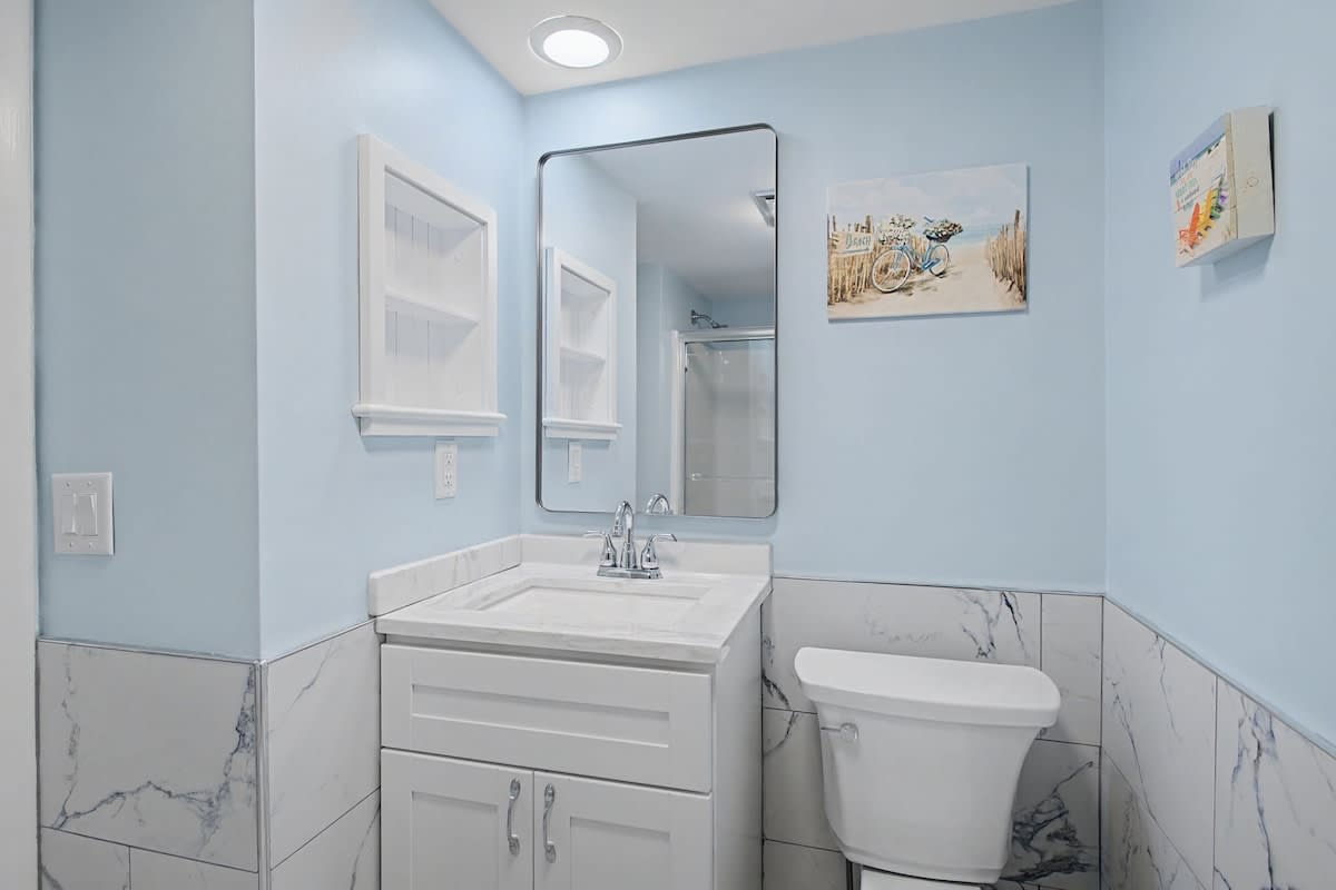 You'll love this bright, coastal-themed bathroom with elegant marble accents, thoughtful storage, and beach artwork that makes every morning feel like a getaway.