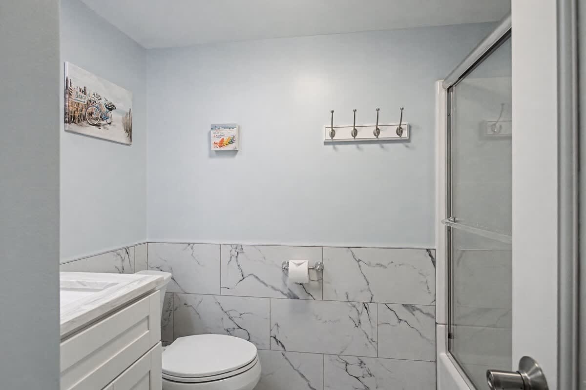 Step into your elegantly updated bathroom featuring marble-look tile, modern fixtures, and thoughtful touches like wall hooks for your convenience.