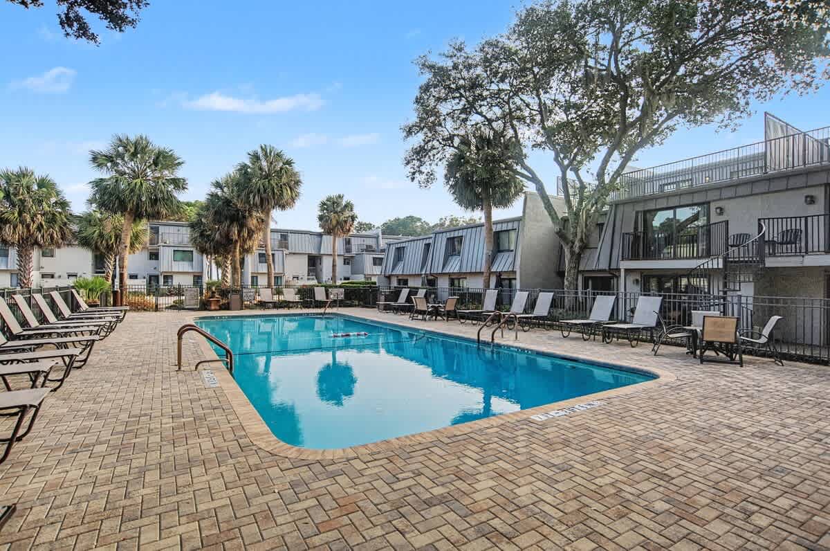 The property features a sparkling outdoor pool surrounded by comfortable loungers beneath swaying palm trees.