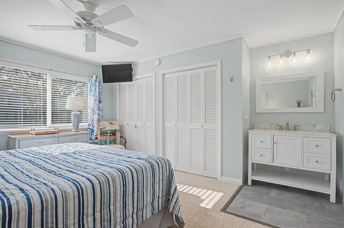 Your peaceful bedroom retreat features coastal charm with blue striped linens, workspace nook, and elegant ensuite vanity for ultimate comfort.