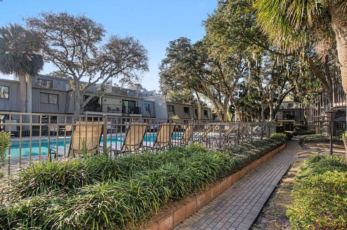 Property walkway leads through landscaped gardens toward the pool area, surrounded by mature trees and tropical plantings.