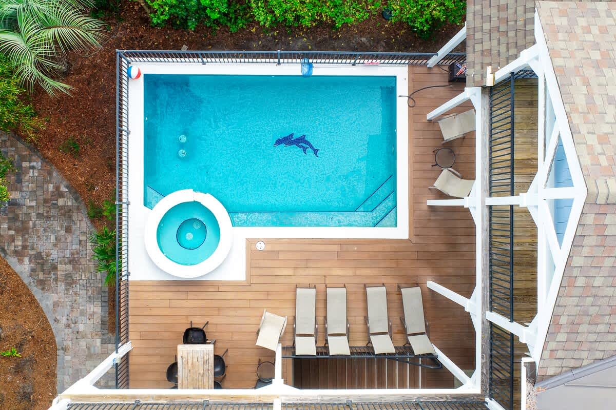 Your private pool awaits with crystal-clear water and a separate hot tub, surrounded by comfortable lounge chairs on warm wooden decking.