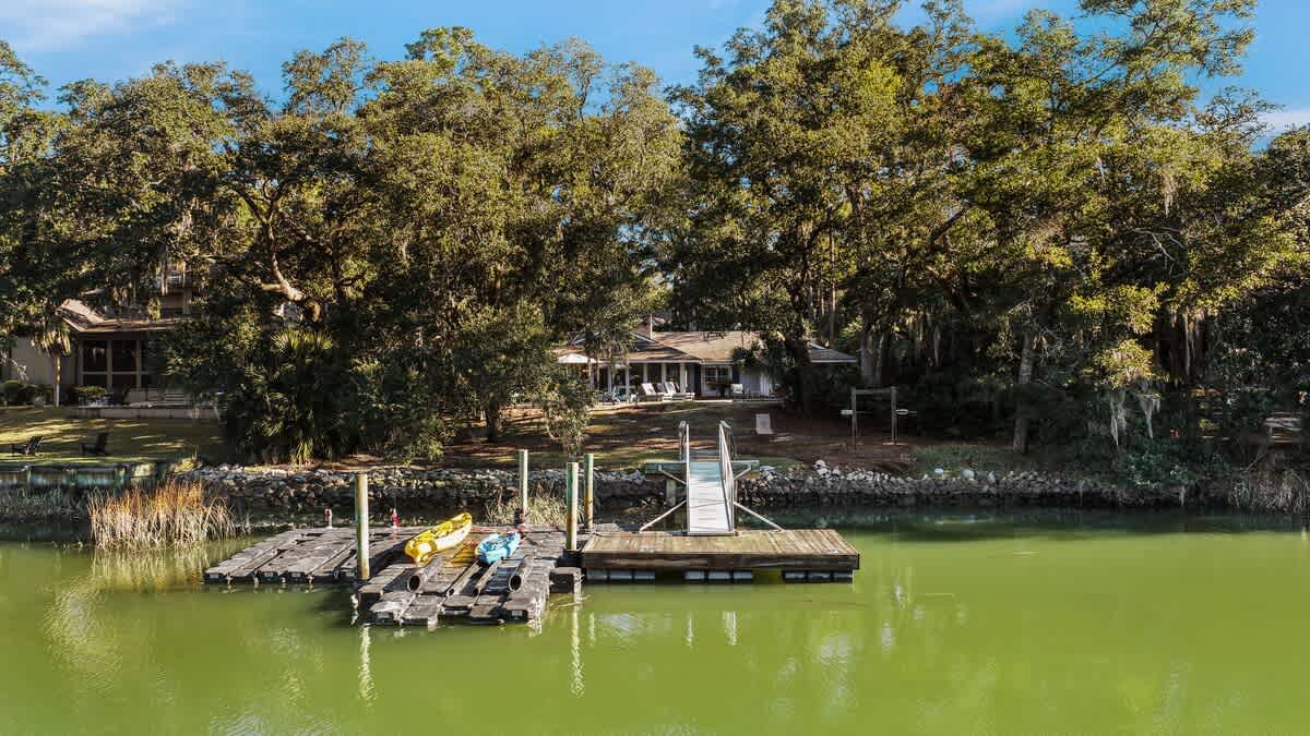 Waterfront property with private dock and kayaks on serene lake surrounded by mature trees.