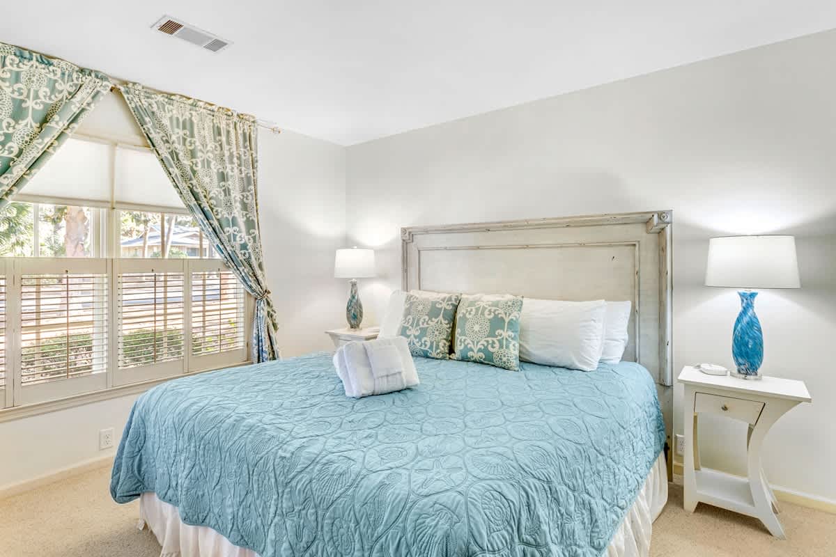 Drift off in this serene bedroom with soft blue linens, natural light streaming through plantation shutters, and coastal-inspired décor.