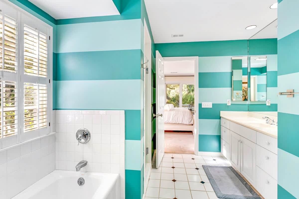 Refresh in your vibrant turquoise-striped bathroom with white tiled tub, dual vanity, and tropical garden views through plantation shutters.