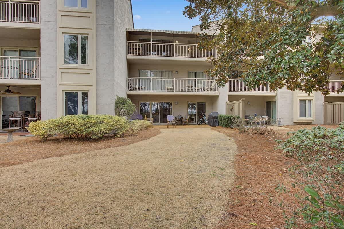 Multi-story condominium complex with ground-floor patios and balconies, surrounded by mature landscaping and open lawn areas.