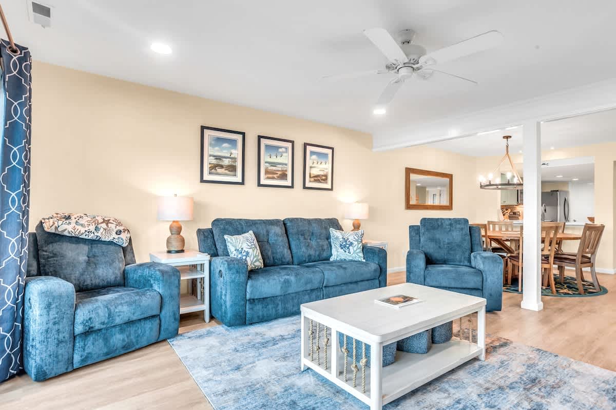 Settle into your spacious living room with plush blue seating and coastal artwork, perfect for relaxing after beach adventures.