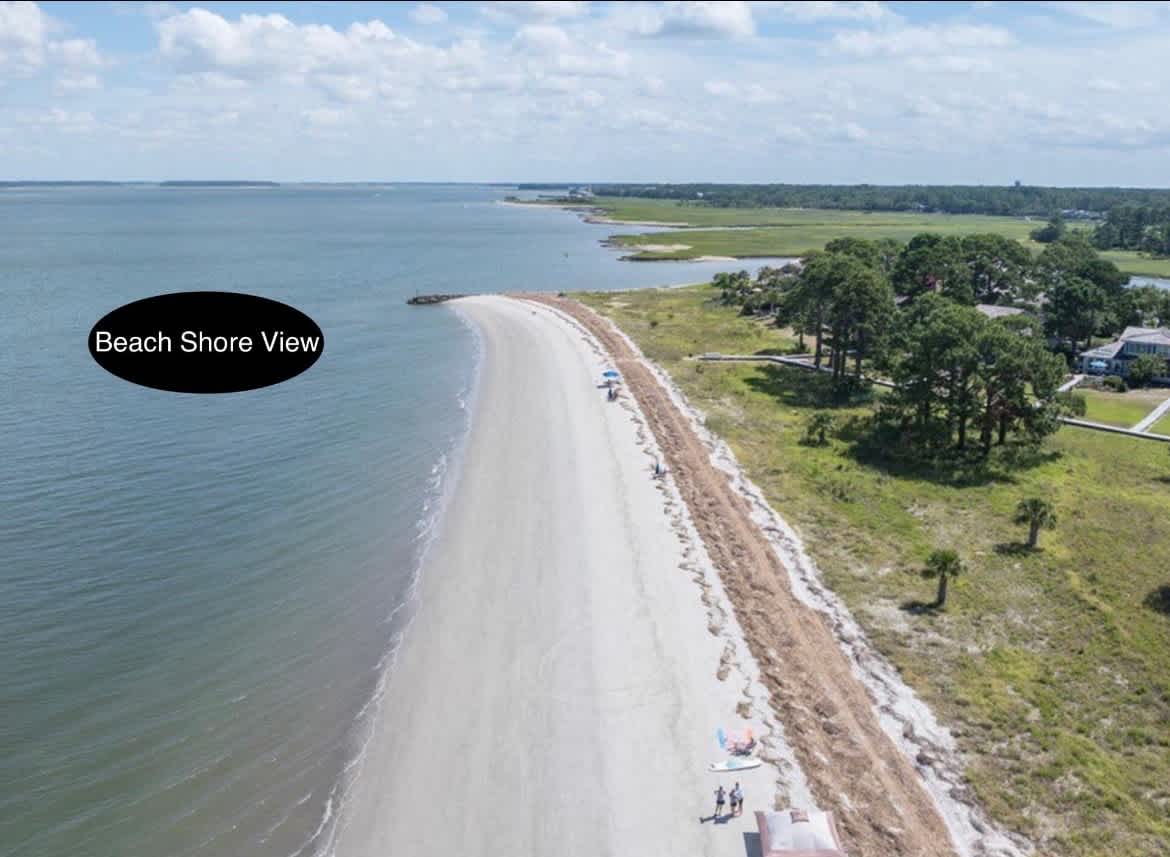 Aerial view of pristine sandy beach stretching along calm waters, with lush coastal landscape and nearby amenities.