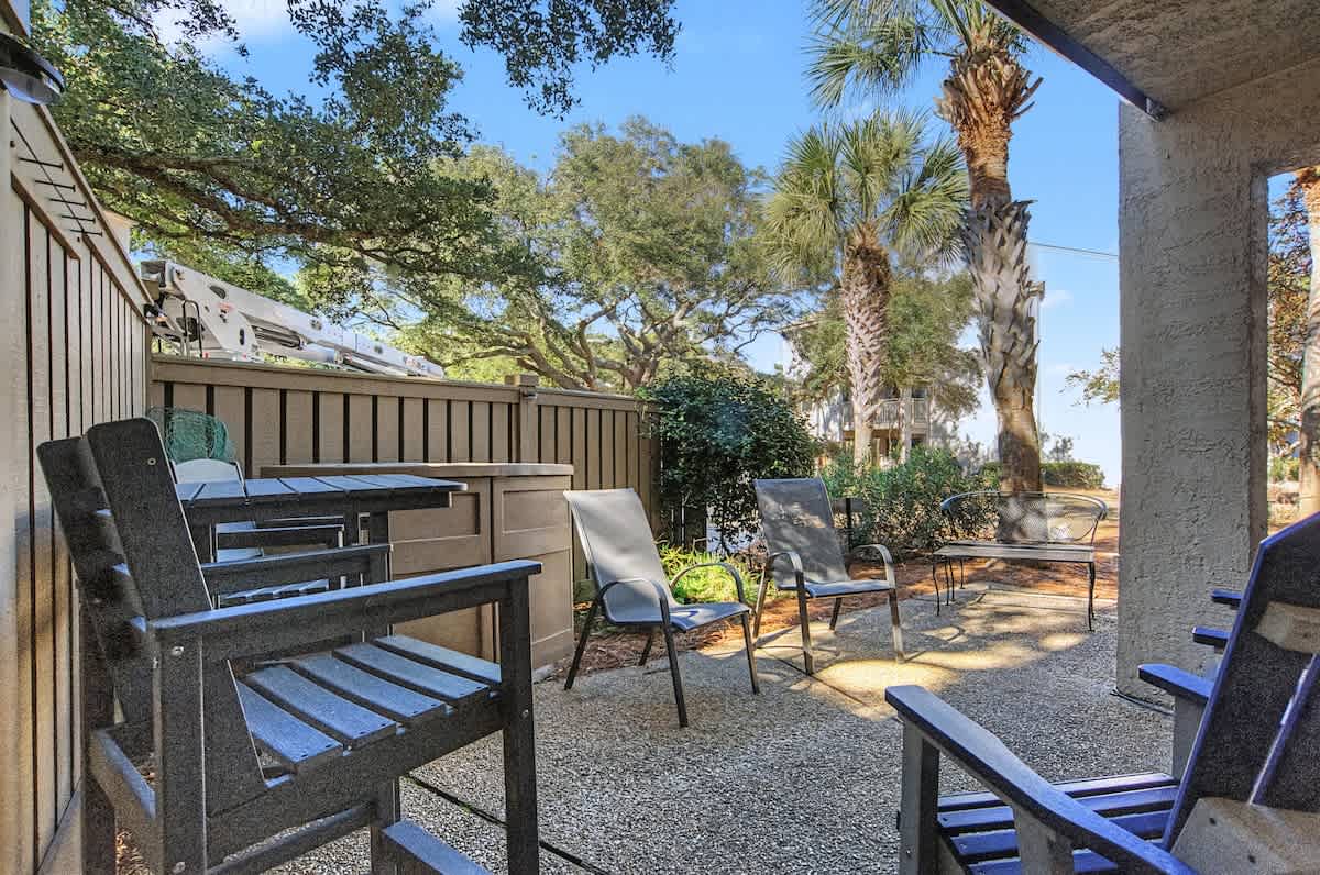 Your private covered patio features comfortable seating surrounded by lush landscaping and mature palm trees.