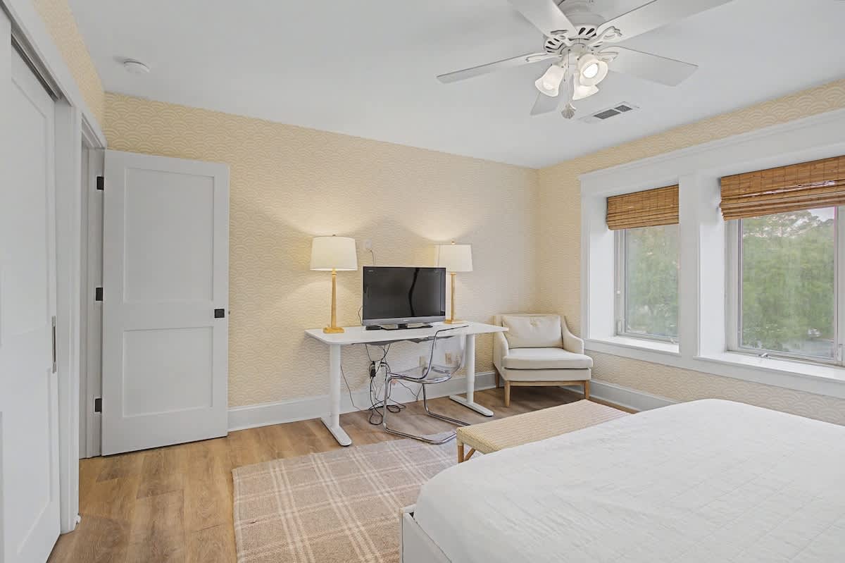 Unwind in your serene bedroom retreat with cozy seating, entertainment center, and peaceful garden views through bamboo shades.