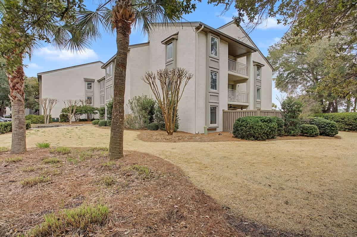 Modern three-story vacation rental building nestled among mature palm trees and lush landscaping in a peaceful residential setting.