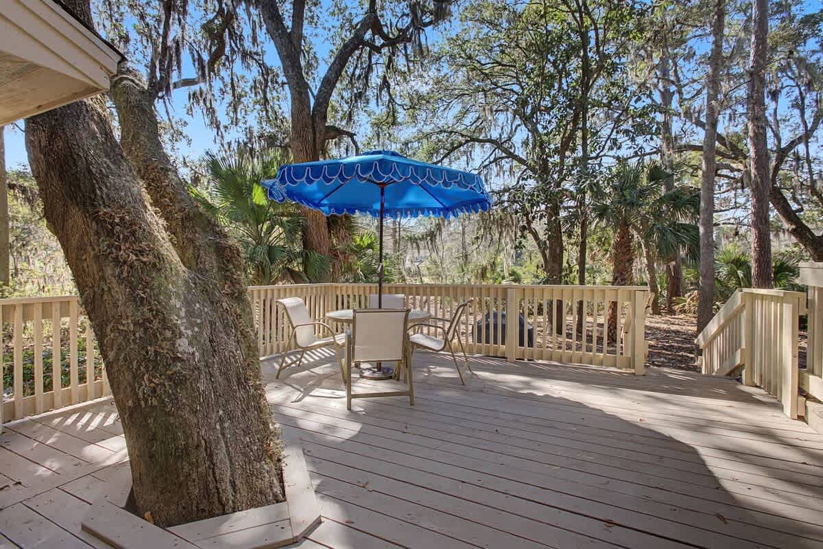 Relax on your private deck surrounded by majestic oaks, where dappled sunlight and a colorful umbrella create the perfect outdoor retreat.