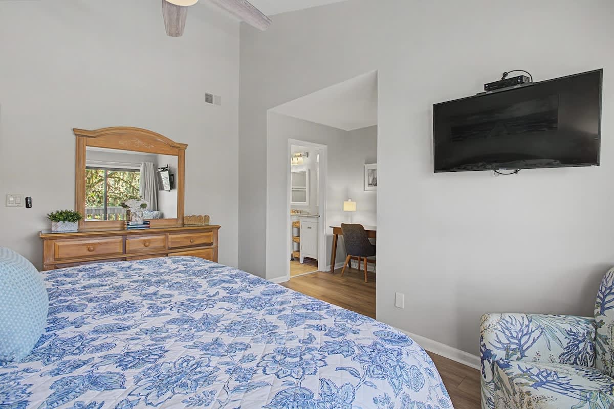 Drift off in your cozy bedroom featuring a plush blue floral bed, warm wood furnishings, and wall-mounted TV for relaxing evenings.