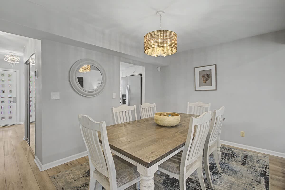 Gather around your elegant dining table where warm conversations flow under coastal-inspired chandelier light and soft natural tones create perfect dinner memories.