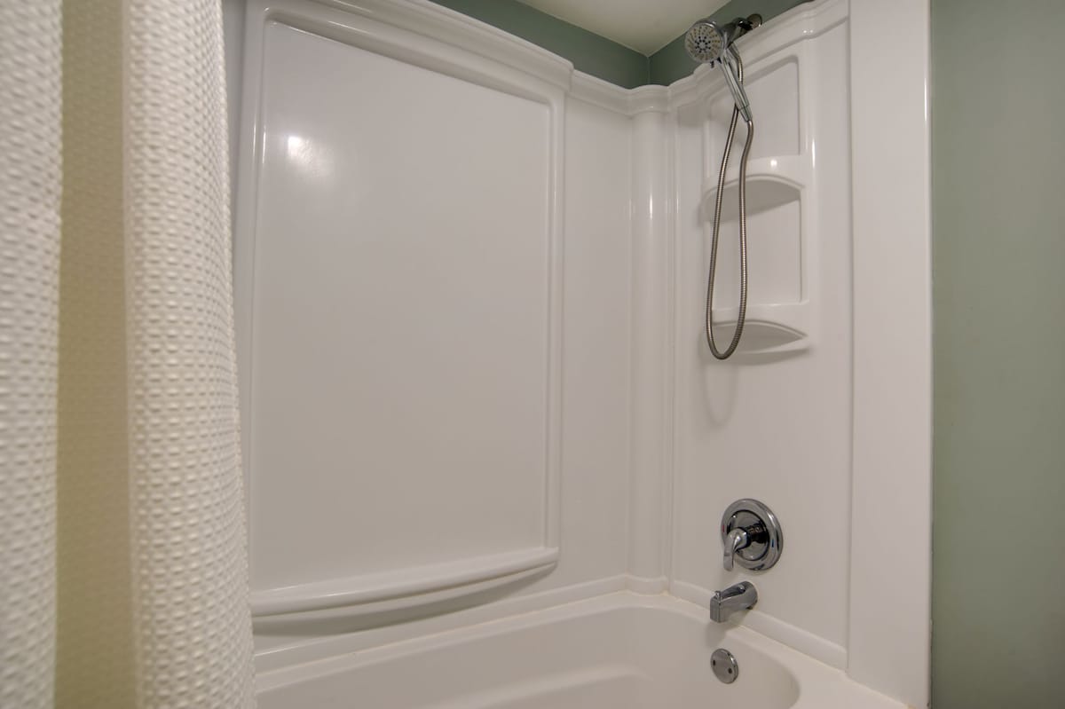 Unwind in your pristine white tub-shower combo with handheld showerhead and convenient corner shelves for toiletries.