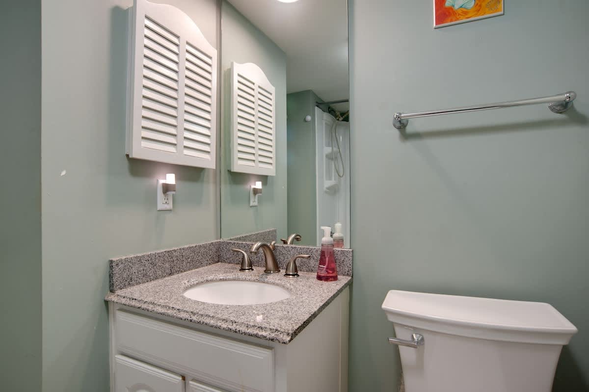 Your private bathroom features granite countertops, white cabinetry, and soothing mint green walls that create a refreshing coastal vibe.